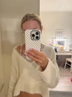 Vit fluffig stickad tröja - Mysig vit stickad tröja med v-ringning och avslappnad passform. Tröjan har breda ribbade muddar och är gjord i ett fluffigt material som känns riktigt mjukt. Perfekt för lager på lager och ger en chill vibe.