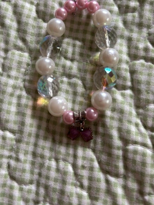 Sött pärlarmband med lila rosett - Ett gulligt armband med stora vita och rosa pärlor samt genomskinliga facetterade pärlor. Armbandet har en liten lila rosettberlock som detalj. Perfekt för dig som gillar söta accessoarer och vill addera lite färg till din stil.