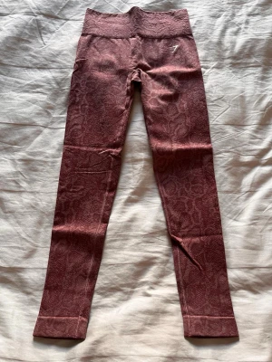 Rosa mönstrade seamless leggings - Säljer ett par rosa seamless leggings med diskret ormmönster och hög midja. De har en tight passform och är tillverkade i ett stretchigt material som ger bra rörelsefrihet. Perfekta för träning eller chill dagar. Liten logga på höften.