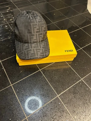 Svart keps med Fendi-logga - INGÅR BOX OCH PRISLAPP!             Snygg svart keps från Fendi med det klassiska FF-monogrammet över hela kepsen. Kepsen har böjd skärm och justerbar baksida. Tillverkad i ett slitstarkt tyg som ger en exklusiv känsla. Perfekt accessoar för dig som gillar lyxiga detaljer.