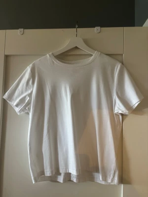 Klassisk vit t-shirt  - En enkel och stilren vit t-shirt med rund hals och korta ärmar. Tillverkad i mjuk bomull som känns skön mot huden. Passar perfekt till alla typer av outfits och har en rak passform. Söm längs ryggen ger en liten extra detalj.
