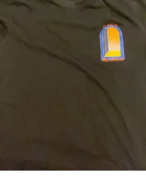Svart t-shirt med färgglatt tryck - Cool svart t-shirt med ett färgglatt grafiskt tryck på bröstet där det står 'Casa Blanca'. Trycket har blå, gul och orange toner och ger en unik vibe. Perfekt för dig som vill sticka ut lite extra.