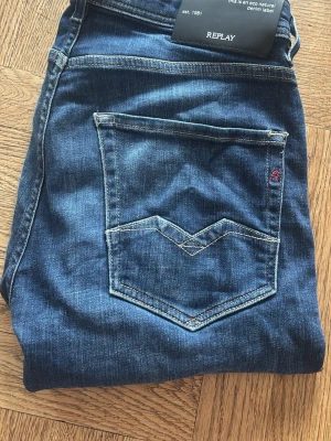 Mörkblå jeans från Replay - Snygga mörkblå jeans från Replay med klassisk femficksmodell och kontrastsömmar. Jeansen har en rak/slim passform och är tillverkade i ett mjukt denimtyg. Bakfickan har en unik detaljsöm och liten röd logga. Perfekta för en avslappnad och trendig stil. Säljer dessa pga har vuxit ur.