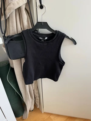 Svart ribbad croppad linnetopp ONLY - Säljer en svart croppad linnetopp från ONLY i ribbad bomull. Toppen är ärmlös och har en rund halsringning. Perfekt att styla med höga jeans eller kjol för en trendig look. Använd en gång. Nypris 149 kr.