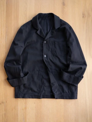 Filippa K Black Chore Jacket, size M - Stilren svart kavaj med tre framfickor och två knappar framtill. Klassisk krage och långärmad modell. Tillverkad i bomullstyg som ger en avslappnad men ändå snygg look. Perfekt för dig som gillar minimalistisk stil. Saknar några knappar på framsida och ärmar, men lätt att hitta liknande om man vill ha det. Personligen använde jag utan. 