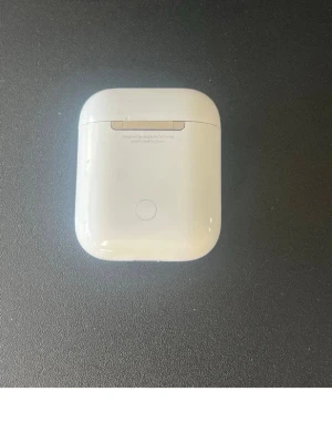 Vit trådlös hörlursfodral - Säljer ett stilrent vitt fodral till trådlösa hörlurar. Fodralet är kompakt, har rundade kanter och är gjort i blank plast. Perfekt för att skydda och ladda dina hörlurar smidigt i fickan eller väskan.
