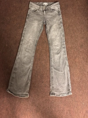 Grå bootcut jeans med broderade fickor - Snygga grå bootcut jeans med broderade detaljer på bakfickorna. Jeansen har klassisk femficksmodell, normal midja och är tillverkade i ett mjukt denimtyg. Perfekta för dig som gillar en avslappnad men trendig look.