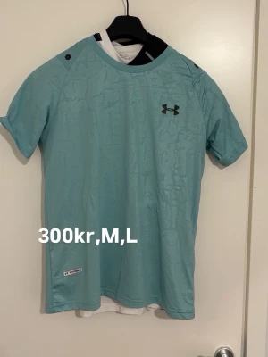 Ljusblå tränings-tshirt Under Armour - Säljer en ljusblå tränings-tshirt från Under Armour med korta ärmar och rund hals. Tillverkad i ett lätt och ventilerande funktionsmaterial, perfekt för gym eller löpning. Diskret logga på bröstet och liten etikett nertill.