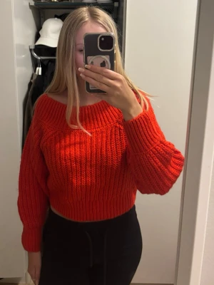 Röd croppad stickad tröja - Snygg röd stickad tröja med croppad passform och bred ribbstickning. Tröjan har en bred, nedhasad urringning och långa ärmar med ribbade muddar. Perfekt för att lyfta vilken outfit som helst.