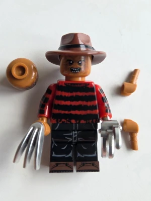 Freddy Krueger minifigur maskerad - Unik minifigur inspirerad av Freddy Krueger med brun hatt, röd- och svart-randig tröja, svarta byxor och metallklor. Inkluderar extra armar, huvud och svart displayplatta. Perfekt till maskerad eller cosplay. Kompatibel med Lego.