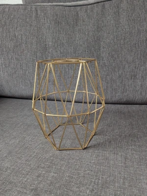 Guldig geometrisk metalllykta - Säljer en stilren ljuslykta i guldig metall med geometriskt mönster. Perfekt som inredningsdetalj på bord eller hylla. Den öppna designen ger ett modernt och luftigt intryck och passar till värmeljus eller små blockljus. Mått: 20x17