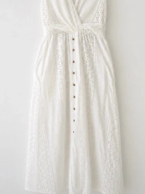 XS Vit långklänning med knappar - Superfin vit långklänning med broderade detaljer och v-ringad omlottliv. Klänningen har knappar framtill och är ärmlös, perfekt för varma dagar. Lätt och luftig känsla med romantisk touch.