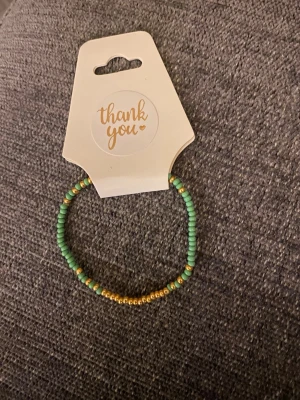 Grönt och guldigt pärlarmband - Snyggt armband med små gröna och guldfärgade pärlor i enkel design. Perfekt för att ge en färgklick till din outfit. Elastiskt band gör det lätt att ta på och av.