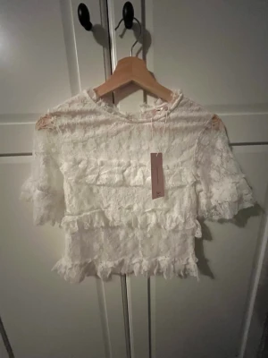 Vit spetsblus med volanger - Supersöt vit blus i spets med volangdetaljer och korta ärmar. Blusen är croppad och har en romantisk känsla med genombruten spets och rund hals. Perfekt för dig som vill ha en feminin och trendig topp till sommaren. Går att diskutera pris💕
