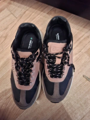 Björn Borg sneakers i svart och beige - Snygga sneakers från Björn Borg i svart, beige och grått med coola svarta och vita snören. Ovandelen är i en mix av mocka och textil, med tydliga paneler och logga på plösen. Perfekta för dig som vill ha en sportig och trendig look.