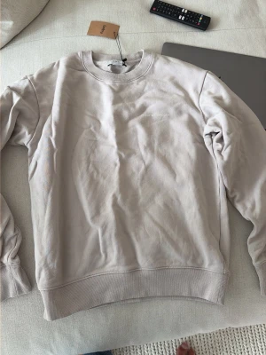 Beige sweatshirt från Tiger of Sweden - Snygg beige sweatshirt från Tiger of Sweden med diskret logga på bröstet. Tröjan har rund halsringning, ribbade muddar vid ärmslut och nederkant samt är tillverkad i mjuk bomull. Perfekt för en avslappnad och stilren look.