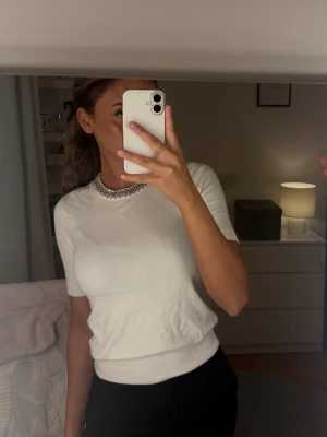 Vit ribbad topp med kort ärm - Säljer en stilren vit topp med ribbade detaljer i midjan och vid ärmsluten. Toppen har korta ärmar och en rund halsringning.