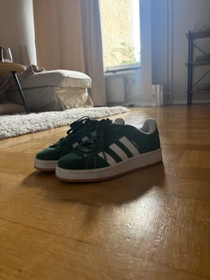 Gröna Adidas Campus sneakers - Säljer mina gröna Adidas Campus sneakers i mocka med klassiska vita ränder på sidorna och vit sula. Använda fåtal gånger.