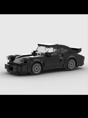 LEGO Porsche 911 Turbo (930) - Säljer en detaljerad sportbil byggd av svarta LEGO-bitar med gråa fälgar och genomskinliga rutor. Bilen har en klassisk coupéform, stora framlyktor och en bakspoiler. Perfekt för dig som gillar bilar och LEGO-byggsatser. Även perfekt för dig som bara vill ha snygg inredning på en hylla eller ett skrivbord. 