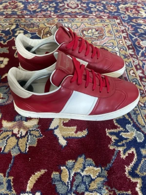 Röda Valentino Flycrew  - Snygga sneakers i rött och vitt med klassisk låg profil. Skorna har ovandel i läder, vita detaljer på sidan och häl samt matchande röda skosnören. Yttersulan är vit och ger en fräsch kontrast till resten av skon. Perfekta för dig som vill sticka ut med stil.