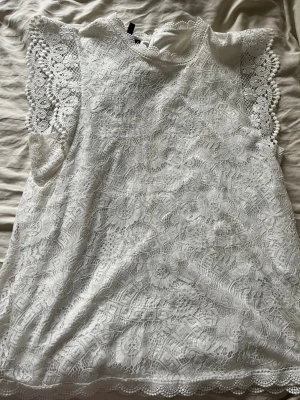 Vit spetsblus från Pieces - Supersöt vit blus från Pieces i spets med fina virkade detaljer och rund hals. Blusen är ärmlös och har ett vackert mönster över hela tyget samt knapp i nacken. Använd någon enstaka gång vilket kan märkas lite på den men ändå väldigt omhändertagen. Köpt på jeansbolaget för typ 400kr något sånt. Den är mer creamvit än vanlig vit men en väldigt fin blus som tyvärr inte kommer till användning. 