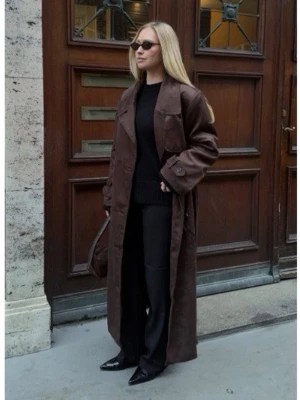 Brun lång trenchcoat i mocka - Snygg brun trenchcoat i mocka. Helt ny, aldrig använd. Storlek 32, ordinarie pris på 1099. Kappan har klassiska detaljer som axelklaffar, stora fickor och bälte i midjan. Perfekt för dig som vill ha en trendig och tidlös look.