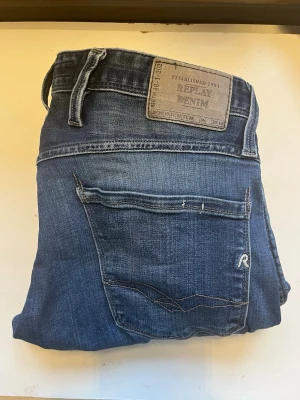 Blå jeans från Replay Denim w30 L32 - Snygga blå jeans från Replay Denim med klassisk femficksdesign och raka ben. Jeansen har en tydlig Replay-logga på bakfickan och patch i läderimitation vid linningen. Tillverkade i slitstark denim med lätt tvättad look.