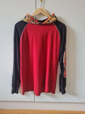 Röd hoodie med flames på huva och ärmar från Kappahl strl 170 barn - Röd hoodie med svarta ärmar och coola flames-motiv på både huva och ärmar. Långärmad modell med kontrastfärgade detaljer. Material 100% bomull. Storlek 170.