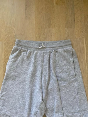 Grå mjukisshorts med snörning - Säljer ett par ljusgrå mjukisshorts med resårmidja och snörning. Shortsen har sidofickor och är tillverkade i mjukt bomullsmaterial, perfekta för chill dagar eller träning. Enkel och clean design som passar till det mesta.