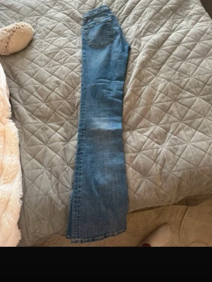 Blå bootcut jeans med hög midja - Säljer ett par klassiska blå bootcut jeans med låg midja och femficksmodell. Jeansen har en snygg tvätt och raka ben som slutar i en lätt utsvängning. Perfekta till sneakers eller boots för en avslappnad look. Använda 2-3 gånger från Zara i storleken 34