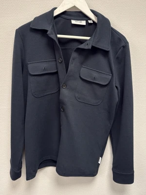 Mörkblå overshirt från Only & Sons - Stilren mörkblå overshirt från Only & Sons i mjukt material. Passar ca 173-183.  Skjortan har två stora bröstfickor med lock och knappar framtill. Klassisk krage och långa ärmar ger en clean look som funkar till många outfits. Skriv för frågor!