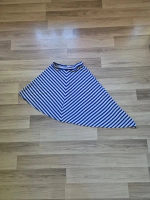 Blåvit randig kjol från Catwalk - Säljer en blåvit randig kjol från Catwalk med sned asymmetrisk form. Kjolen har bred resår i midjan och är gjord i ett mjukt, stretchigt material som känns bekvämt. Perfekt för dig som gillar en unik och trendig stil.