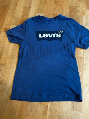 Blå Levi's t-shirt med logga - Snygg blå t-shirt från Levi's med stor vit logga på bröstet. Klassisk passform och rund halsringning. Tillverkad i mjuk bomull som känns skön mot huden. Perfekt för en avslappnad och stilren look. Vid minsta fundering är d bara att skriva 😁