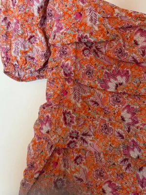 Blommig kortklänning med puffärm - Superfin kortklänning med färgglatt blommönster i orange, rosa och lila toner. Klänningen har puffiga ärmar och en smickrande passform med rynkade detaljer. Storlek L men passar mer M