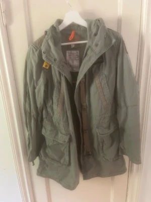 Parajumpers PJS  Flea Market Parka  - Säljer en äkta Parajumpers Flea Market Parka i olivgrönt, storlek M.  Jackan är i mycket fint skick och knappt använd. En lätt och stilren parkas/fältjacka med huva, flera praktiska fickor och Parajumpers klassiska detaljer.  * Skick: Mycket fint, nära nyskick * Originaldetaljer och patch kvar