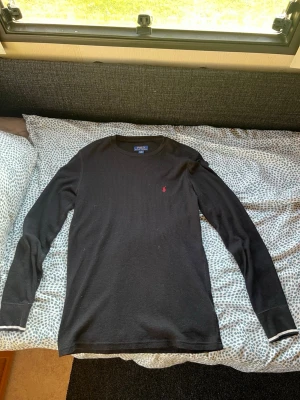 Svart långärmad tröja Polo Ralph Lauren - Svart långärmad tröja från Polo Ralph Lauren i ribbad bomull. Rund hals och liten röd broderad logga på bröstet. Enkel och stilren design som funkar till det mesta.