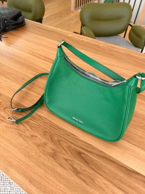 Michael Kors handväska – grön - Snygg och stilren Michael Kors handväska i grön färg, modell MK0230. Klassisk design med silverfärgade detaljer och ett praktiskt handtag.  💚 Färg: Grön 👜 Märke: Michael Kors 📦 Modell: MK0230 ✨ Skick: Mycket fint skick  Nypris ca 4 579 kr.