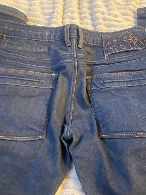 Blå bootcut jeans från DC - Snygga blå jeans från DC med staight fit passform och klassiska fickor. Jeansen har en broderad DC-logga bak i midjan och är gjorda i ett mjukt denimtyg. Perfekta för dig som gillar streetwear och vill ha en avslappnad look.