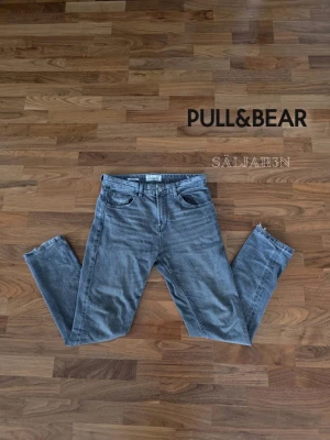 Grå jeans från Pull&Bear - PULL&BEAR Jeans Straight Fit – Storlek 42 (W32) – Fint skick Stilrena Pull&Bear jeans i grå denim med rak straight fit-passform. Klassisk 5-ficksmodell med tidlös look som fungerar lika bra till vardag som till mer uppklädda outfits. Jeansen är i fint skick med naturlig tvättad finish och utan större slitningar eller skador.  ✅ Straight fit ✅ Storlek: EUR 42 (W32) ✅ Grå/blå tvätt ✅ 5-ficksmodell ✅ Fint skick  Perfekt basplagg som passar till allt i garderoben. 📦 Snabb leverans!