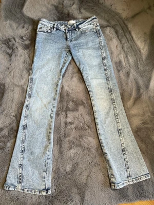 Ljusblå low waist bootcut jeans Gina Tricot  - Säljer ett par ljusblå low waist bootcut jeans med klassisk femficksdesign och dragkedjegylf. Jeansen har en snygg tvättad look och raka ben som går ut lite nertill. Perfekta för en avslappnad och trendig stil.