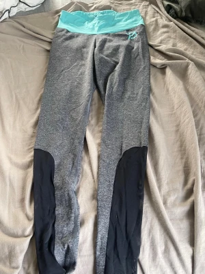 Grå leggings med turkos midja - Snygga leggings i grått med bred turkos midjeresår och svarta detaljer längs benen. Perfekta för träning eller chill, med skön stretch och figurnära passform. 