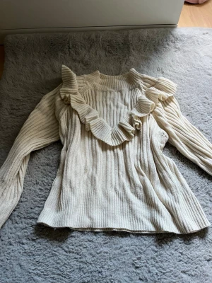 Beige stickad tröja med volang SHEIN - Säljer en beige stickad tröja från SHEIN i storlek S. Tröjan har långa ärmar, ribbad struktur och en snygg volangdetalj som går diagonalt över bröstet och axeln. Perfekt för dig som gillar trendiga detaljer och mjuka material.