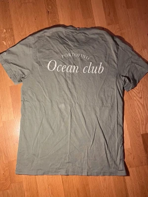 Olivgrön Les Deux T-shirt med tryck - Snygg olivgrön t-shirt från LesDeux, med trycket 'Portofino Ocean club' på ryggen och diskret logga på ärmen. Perfekt för en avslappnad stil och enkel att matcha. Tillverkad i bomull. Nyskick! 💯
