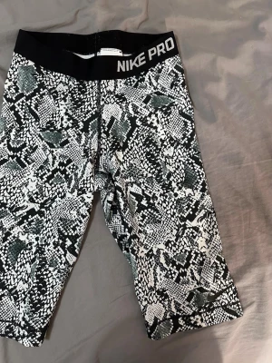 Nike Pro tights med ormmönster - Säljer ett par Nike Pro tights med svartvitt ormmönster och bred svart resår i midjan med Nike Pro-logga. Tightsen är knälånga och tillverkade i ett stretchigt funktionsmaterial som passar perfekt till träning.