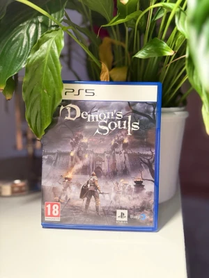 Demon's Souls till PS5 - Säljer spelet Demon's Souls till PlayStation 5. Spelet kommer i ett blått plastfodral med omslag i mörka färger och fantasytema. Inuti finns spelets skiva med en riddare på. Perfekt för dig som gillar action och utmanande äventyr.