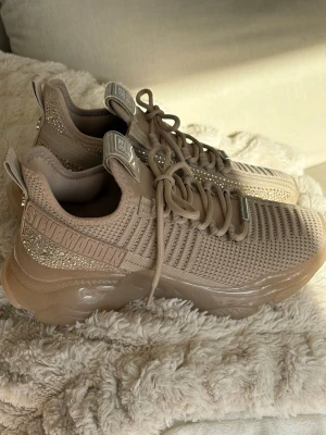 Beige chunky sneakers Steve Madden - Chunky sneakers i beige från Steve Madden med stickad ovandel, glittriga detaljer och tjock sula. Skorna har snörning och logga på plösen samt sidan. Perfekta för dig som gillar streetstyle och vill sticka ut med en trendig look.Storlek 39, endast provade här hemma. 
