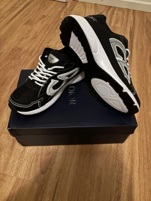 Svarta sneakers med vita detaljer B30 - Snygga svarta sneakers med vita och silverfärgade detaljer samt vita skosnören. Skorna har en chunky vit sula och meshpaneler för extra andningsförmåga. Perfekt för dig som vill ha en trendig och exklusiv look.