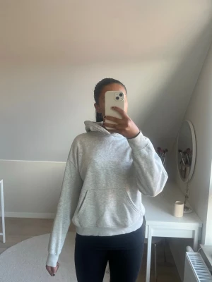 Ljusgrå hoodie med ficka - En stilren ljusgrå hoodie med huva och stor magficka. Hoodien har långa ärmar och ribbade muddar vid ärmslut och nederkant. Perfekt för en avslappnad och bekväm look. Den har tyvärr några sminkfläckar på insidan av huvan men inget som syns annars ☺️