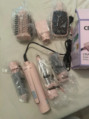 CRASTS 6-i-1 hårstyler rosa - Multifunktionell hårstyler från CRASTS i rosa med sex utbytbara tillbehör, inklusive rundborstar, plattborste och fönmunstycke. Perfekt för att skapa olika frisyrer hemma. Levereras med originalkartong och alla delar i plastförpackning.