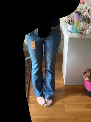 Blå bootcut jeans från Lee - Säljer ett par klassiska blå bootcut jeans från Lee. Jeansen har normalhög midja, fem fickor och är tillverkade i ett mjukt denimtyg. Snygg passform som sitter tajt upptill och släpper ut vid benen. Perfekta till en avslappnad och trendig look.